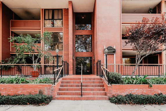 Front view of a multi-story brick building with balconies and stairs leading to the entrance.