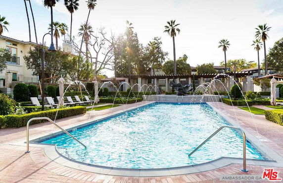 View of an outdoor swimming pool with fountains and surrounding lounge chairs.