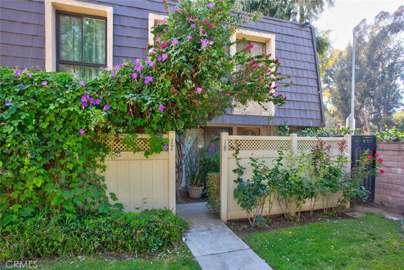 Front view of a residential building with flower-draped facade and fenced entrance.