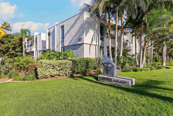 Front view of a modern multi-story building with balconies and lush landscaping.