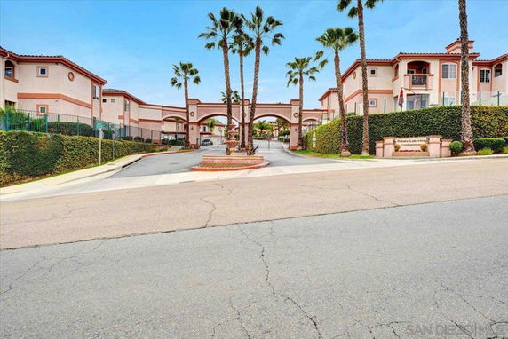 Front view of a two-story residential complex with palm trees and an arched entrance.