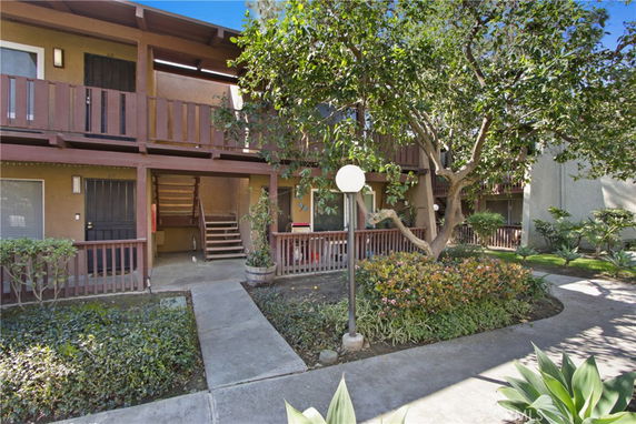 Front view of a two-story residential building with a wooden balcony and surrounding garden.