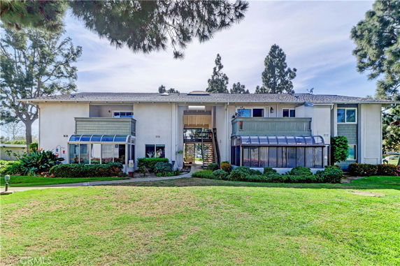 Front view of a two-story house with large glass sunrooms and greenery in front.