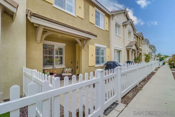 Front view of a two-story townhouse with a porch and white picket fence.