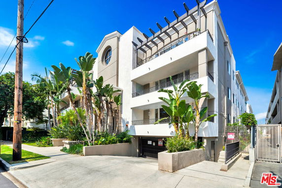 Front view of a multi-story residential building with balconies and lush greenery.