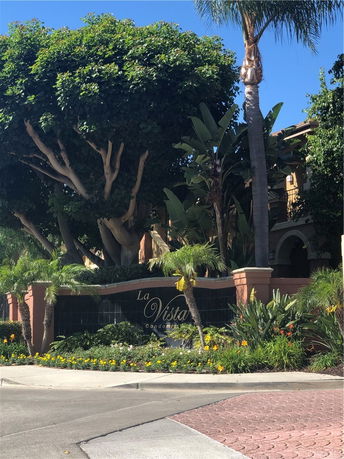 Front view of a condominium entrance with large trees and decorative signage.