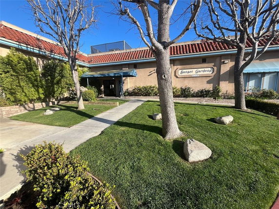 Front view of a building with signage reading 'Sunset Gardens', featuring a pathway and red-tiled roof.