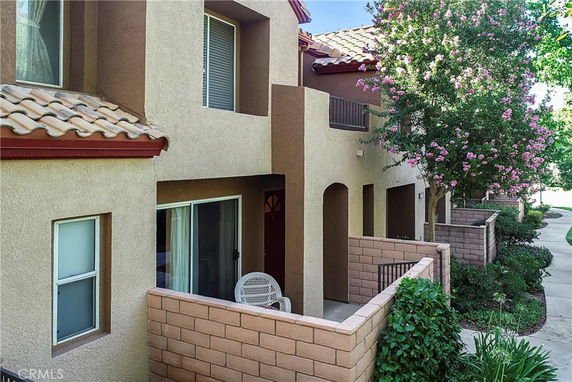 Front view of a multi-story residential building with small patios and tiled roofs.