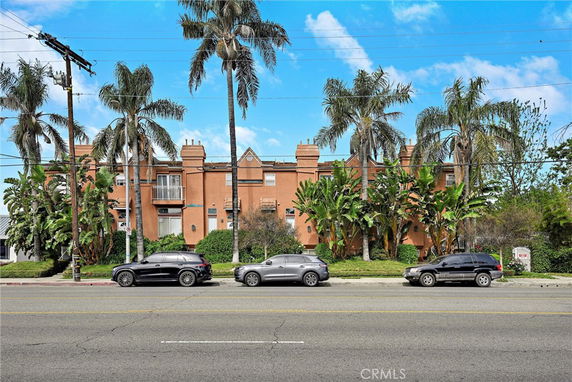 Front view of a two-story building with palm trees and parked cars.