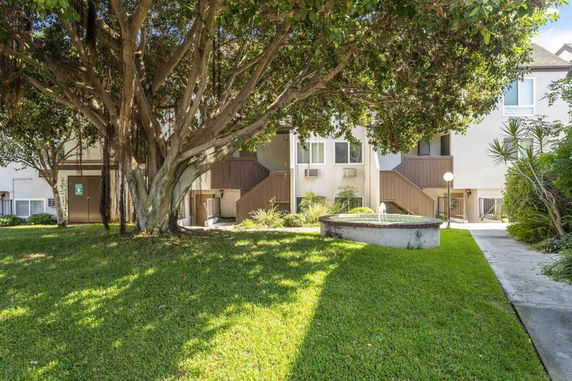 View of a residential building with a tree and fountain in the front yard.