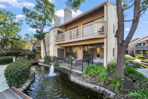 Front view of a two-story house with balconies and a small pond with a fountain.