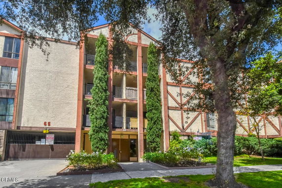 Front view of a multi-story residential building with balconies and large trees.