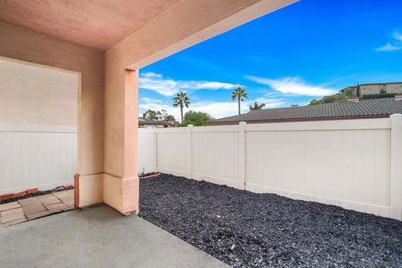 View of a fenced backyard with a paved area and mulch.