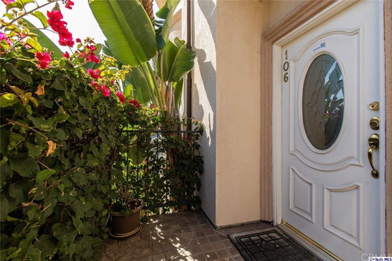 Front entry view of a house with a white door and decorative glass oval, surrounded by plants and flowers.