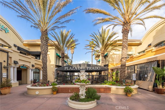 Front view of a shopping center entrance with palm trees and a decorative fountain.