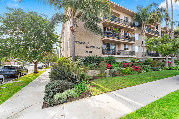 Front view of a multi-story apartment building with balconies and landscaped greenery.
