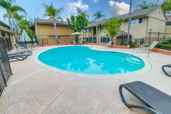 Outdoor swimming pool surrounded by buildings with lounge chairs and umbrellas.