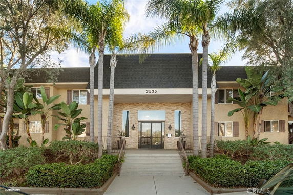 Front view of a two-story building with palm trees and large entrance.