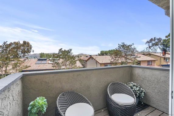 View from a balcony overlooking rooftops with solar panels and distant hills.