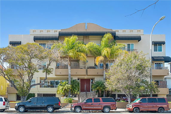 Front view of a multi-story apartment building with palm trees in front.