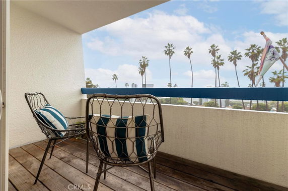 Balcony with two chairs overlooking a scenic view with palm trees.