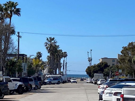 Outdoor street view with parked cars on both sides and a distant view of the ocean.