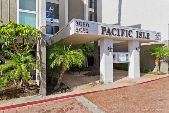 Front view of a building entrance labeled 'Pacific Isle' with an overhang and surrounding palm trees.
