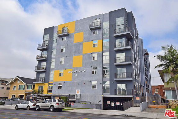 Front view of a multi-story apartment building with balconies and a parking area below.