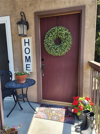Outdoor entrance view with a door adorned by a wreath, a small table with a chair, and decorative plants.