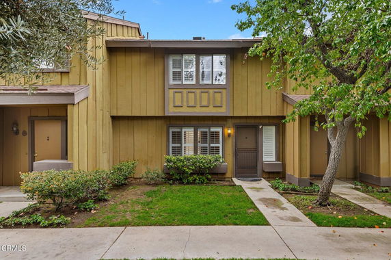 Front view of a two-story townhouse with a brown and beige exterior, featuring a central door and windows with shutters.