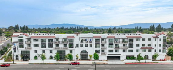 Front view of a multi-story white apartment building with balconies and large windows.