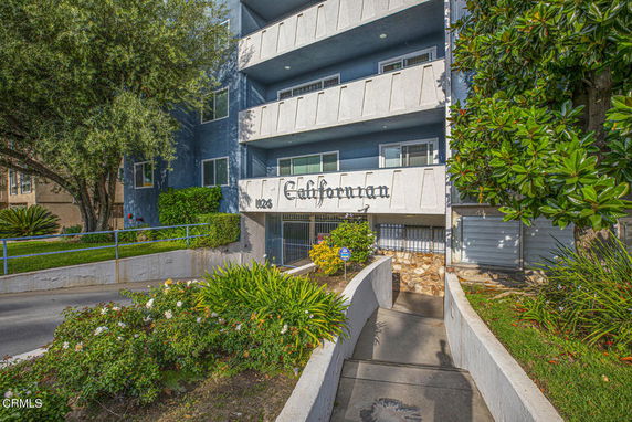 Front view of a multi-story residential building with balconies and an entrance pathway.