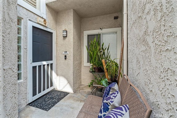Front view of a house entrance with a screen door, plants, and seating area.