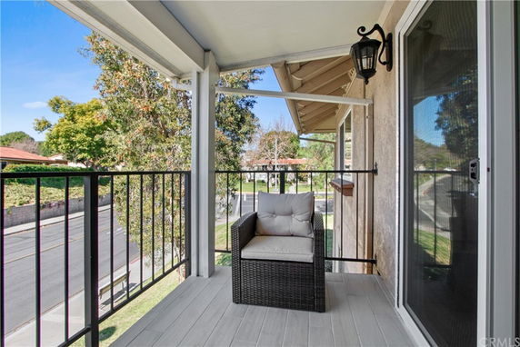 Balcony with railing and a chair, showing view of trees and street.