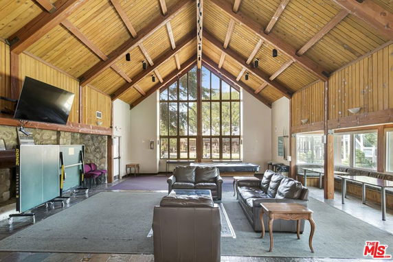 Spacious indoor area with wood-paneled ceiling and large windows, featuring seating and a mounted TV.
