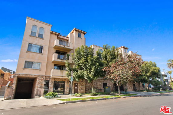Front view of a multi-story apartment building with balconies and a stone facade entrance.