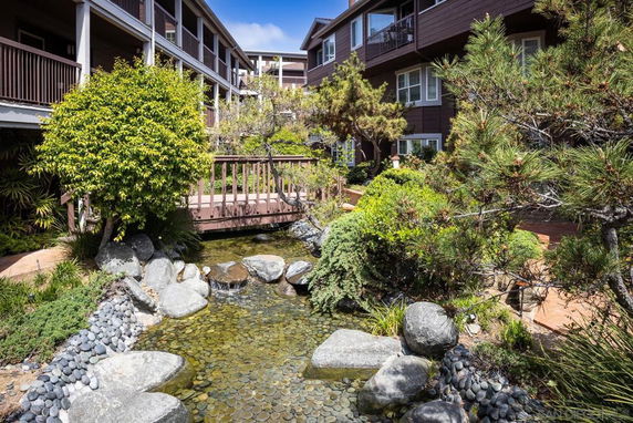 Exterior view of a residential complex with a landscaped garden and a small pond with stones and plants.
