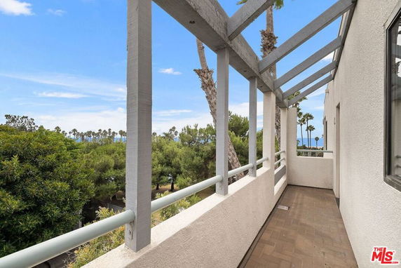 View from a balcony with a railing and pergola, overlooking trees and distant palm trees.