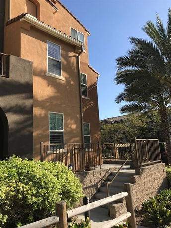 Side view of a multi-story building with tan and brown exterior and a small balcony.