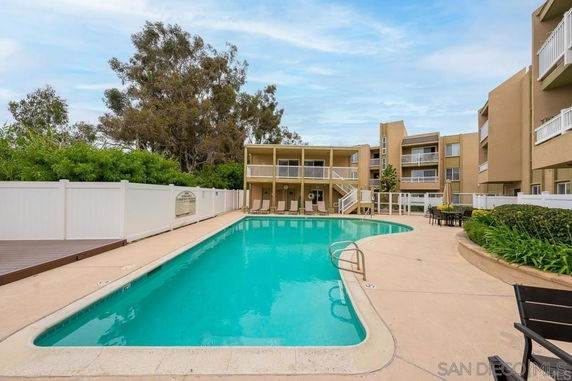 Outdoor swimming pool surrounded by a low-rise building and greenery.