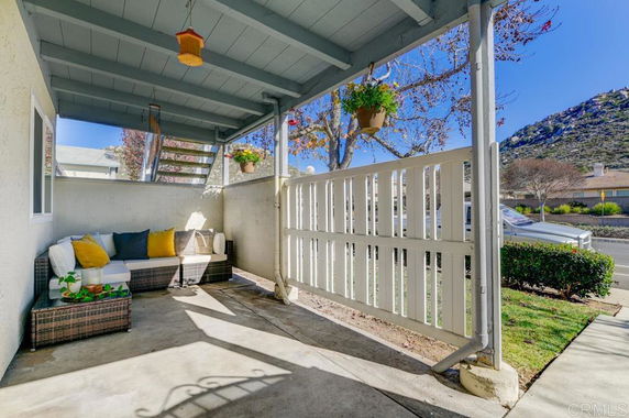 Covered porch area with outdoor seating and fenced view, overlooking a street and hillside.