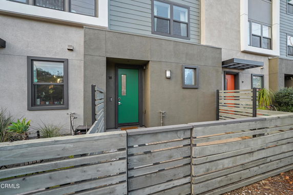 Front view of a modern townhome with a green door and fenced front area.
