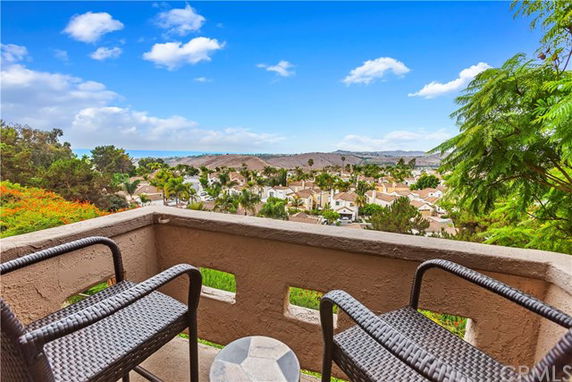 Balcony with chairs overlooking a scenic view of a residential area and distant hills.