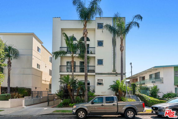 Front view of a multi-story residential building with balconies and palm trees.