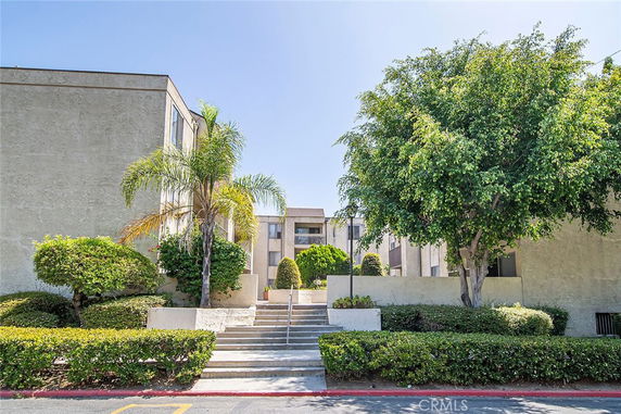 Front view of a multi-story apartment building with steps leading to the entrance and surrounded by trees.
