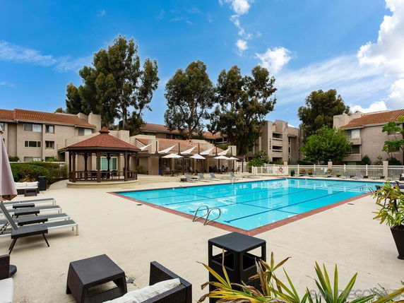 Outdoor area of an apartment complex featuring a large swimming pool surrounded by lounge chairs and a gazebo.