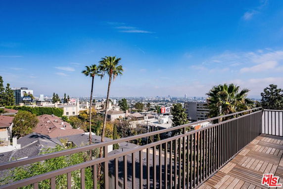 Panoramic view of the city from a building balcony with railing and trees.