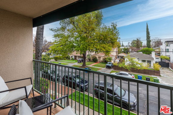 View from a balcony overlooking a residential street with parked cars and houses.