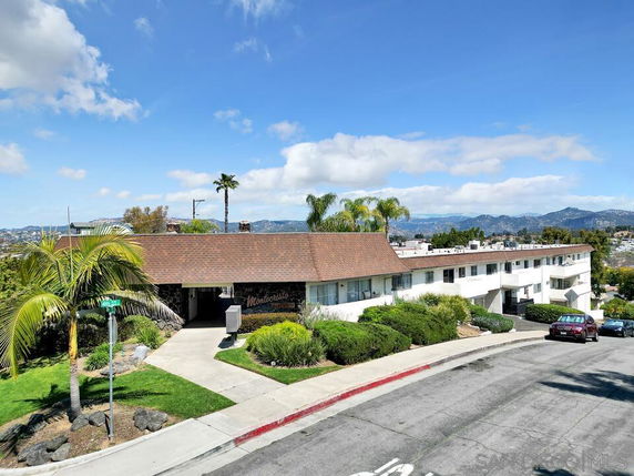 Front view of a two-story building with a sloped roof and surrounding vegetation.