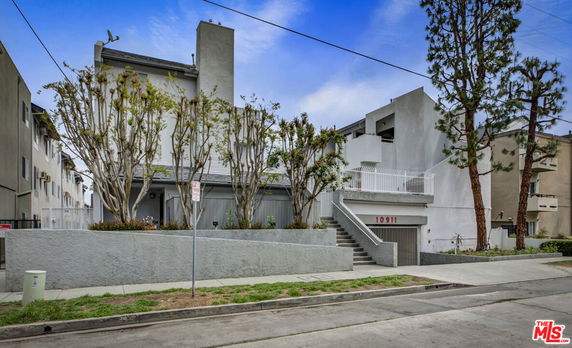 Front view of a multi-story residential building with trees and staircase entrance.
